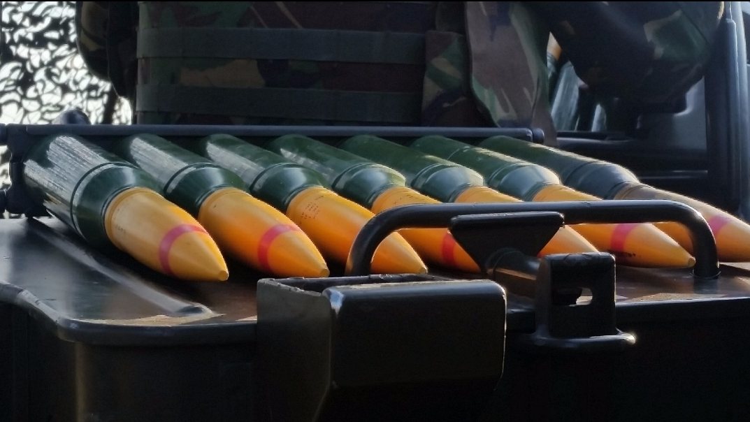 35 mm High Explosive Incendiary rounds laid out on an Oerlikon GDF gun mount in preparation for a live-fire serial. Distinctive yellow-painted ogives with red driving-band stencilling identify the HEI nature of the rounds.