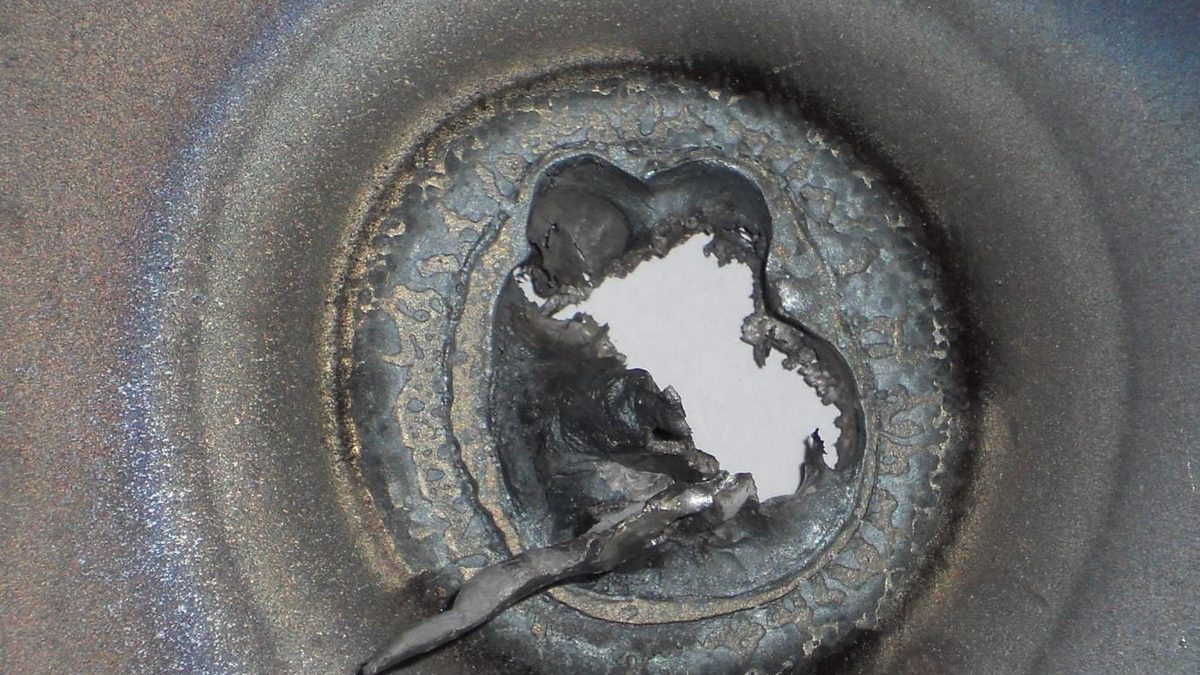 Thermite burn-through aftermath on a thick-cased munition body, showing molten slag at the penetration point.