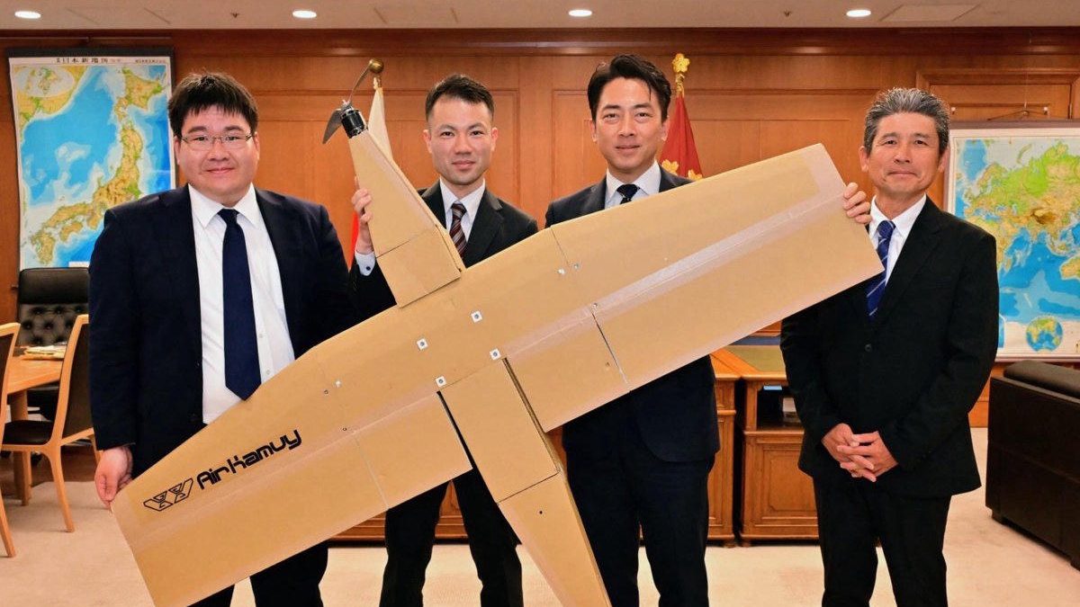 Japan's Defence Minister Shinjirō Koizumi (second from right) and three AirKamuy Inc. executives hold the corrugated-cardboard AirKamuy 150 fixed-wing drone in a Ministry of Defence boardroom, Tokyo, late April 2026.