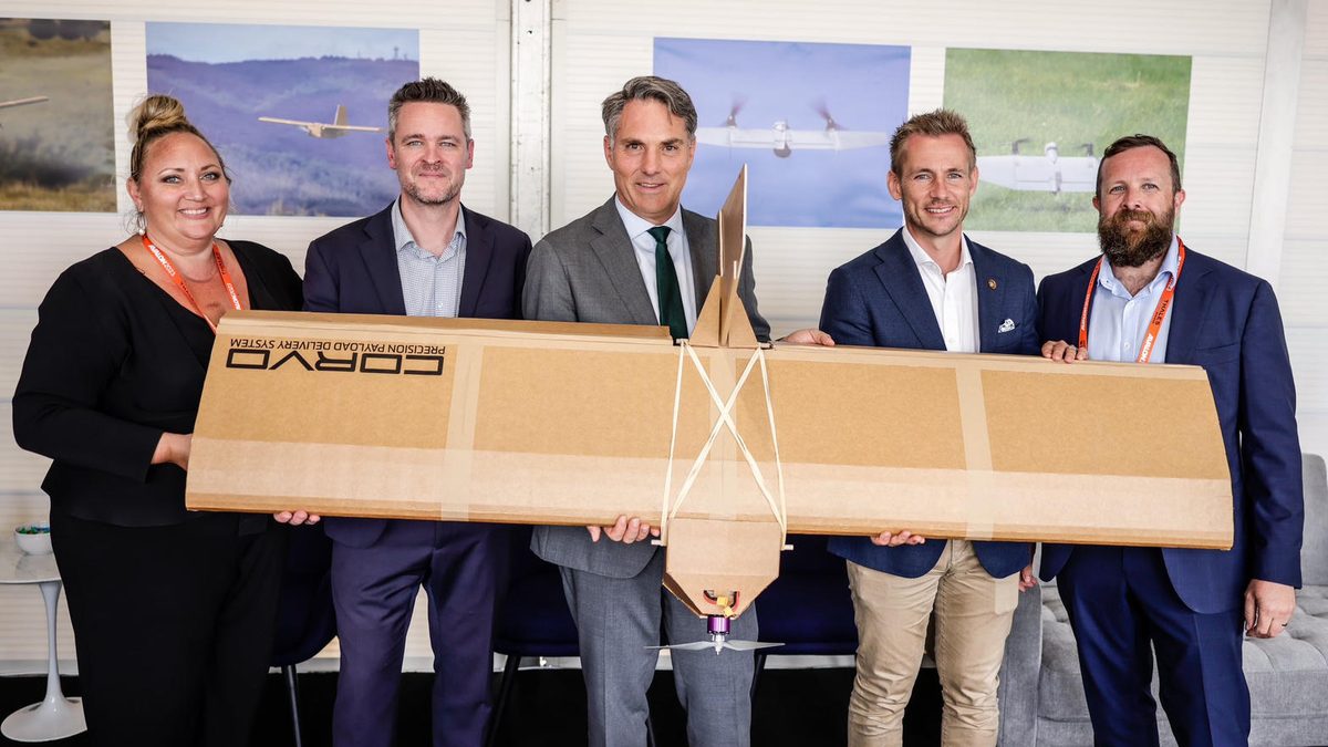 Australian Deputy Prime Minister Richard Marles (centre, grey suit, green tie) with four SYPAQ Systems team members holding the corrugated-cardboard Corvo Precision Payload Delivery System at the SYPAQ stand, Avalon Australian International Airshow 2023.