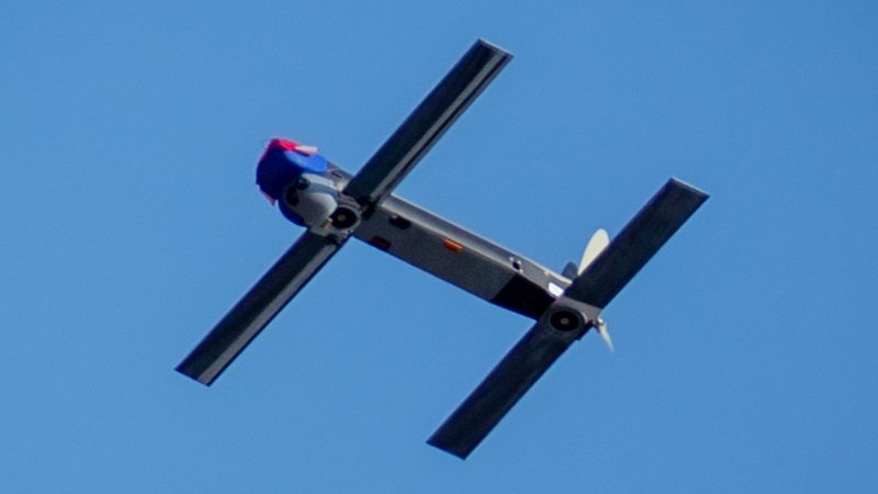 AeroVironment Switchblade 300 loitering munition in flight — twin-boom airframe and cruciform X-wing tail surfaces deployed, propeller turning, photographed against blue sky during a US Marine Corps exercise at Camp Pendleton, California