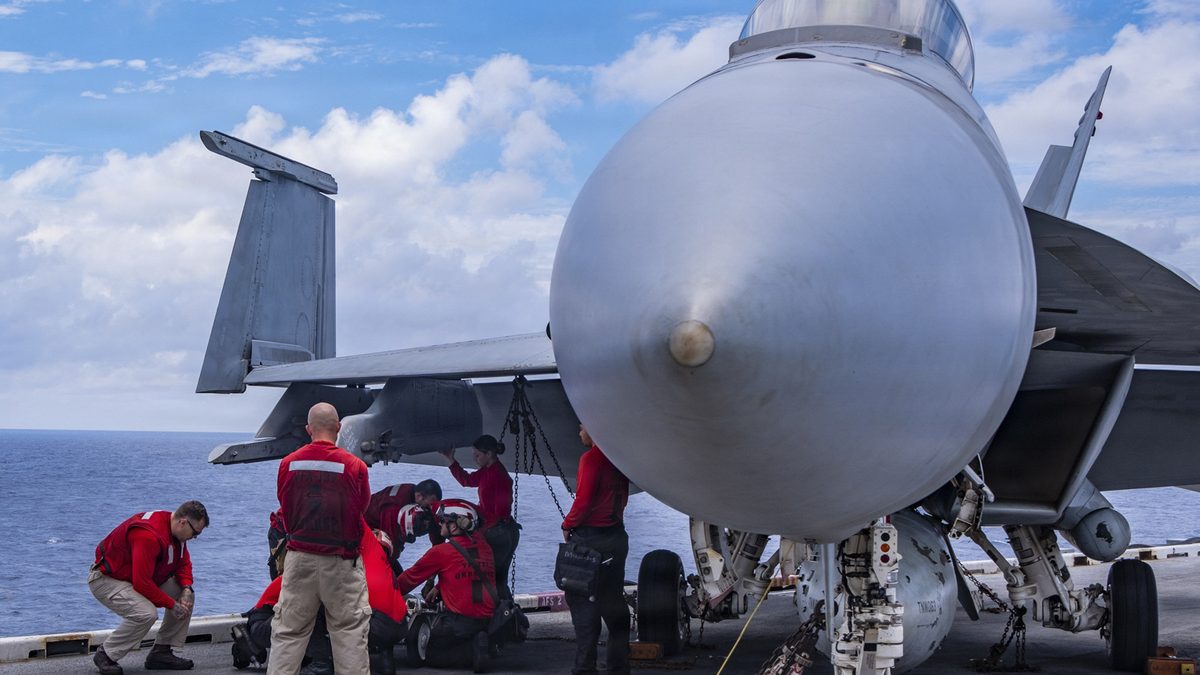 Aviation ordnancemen load ordnance onto an F/A-18E Super Hornet on a carrier flight deck at sea