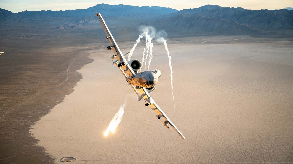 A US Air Force A-10C Thunderbolt II dispenses defensive flares during an evasive manoeuvre over a desert range