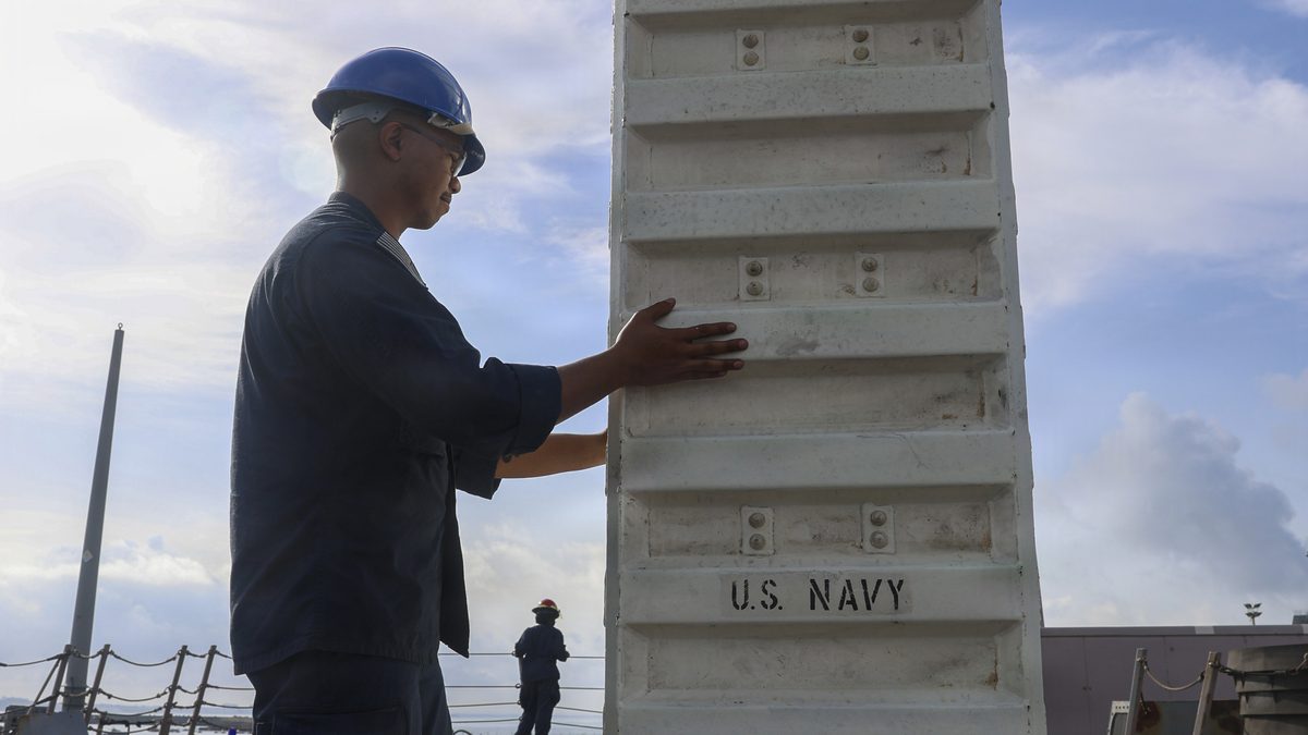 A sailor guides a missile canister into a Vertical Launch System cell aboard USS Oscar Austin