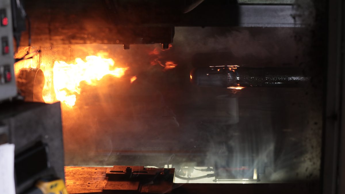 A heated billet being extruded under press during projectile case production