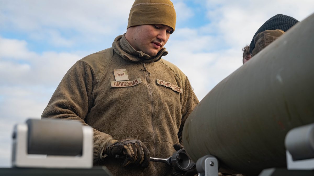 A US Air Force weapons load crew member prepares a fuze well on a munition for fuze installation