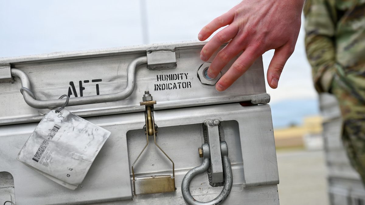 US Air Force Airman's hand beside the humidity indicator on a stencilled aluminium munitions container