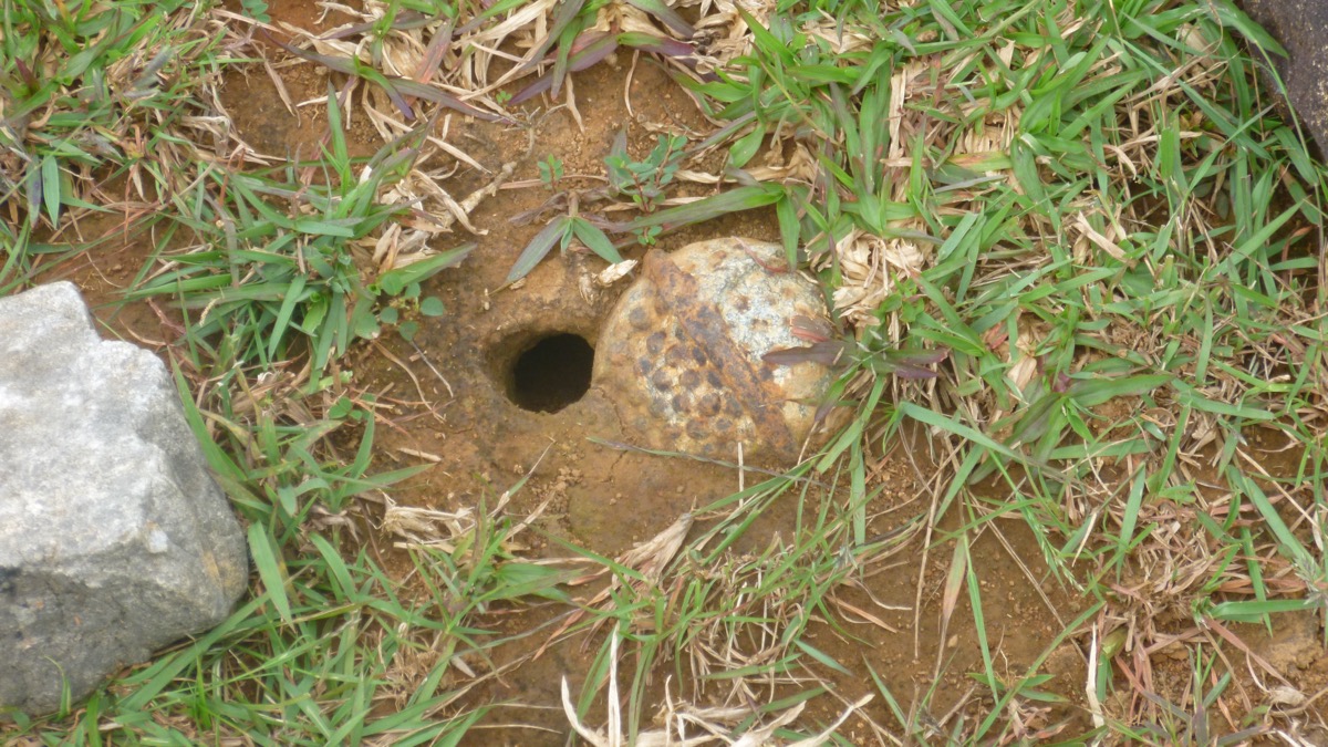 BLU-26 cluster submunition partially buried in ground showing fragmentation pattern